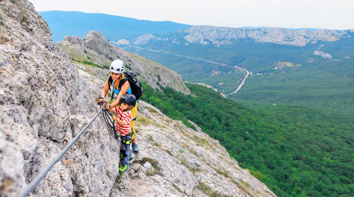 Mother, child in safety equipment climb by via ferrata route